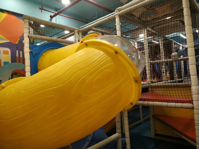 Yellow slide in an indoor playground with colorful structures and nets.