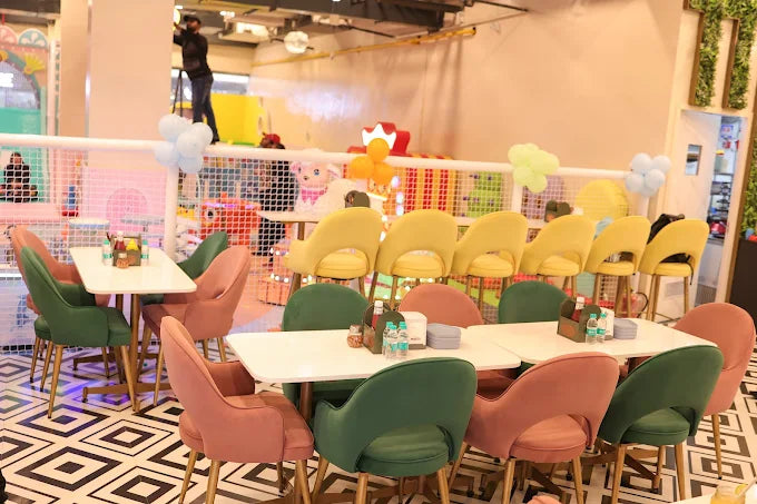 Modern indoor play café with green and pink chairs, yellow barstools, white tables, and playful decorations