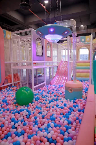 Indoor play area with colorful ball pit, pink slide, and hanging play structure in a modern kids’ zone