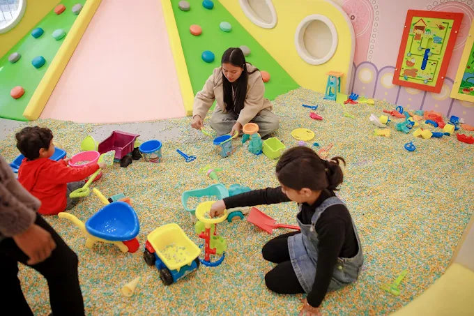Children playing with colorful sand and toy trucks in a lively indoor play area at Tooney Tales Gurugram