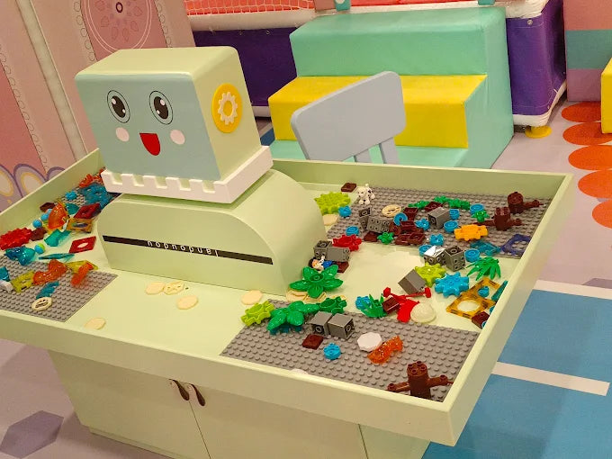 Interactive play table with colorful building blocks and a smiling robot figure in a vibrant children’s activity zone
