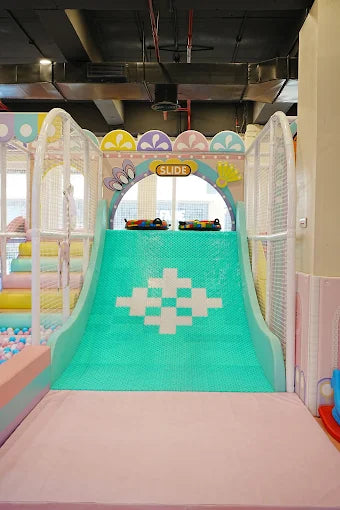 Indoor kids’ play slide with turquoise textured surface and pastel decorative arch in vibrant play area