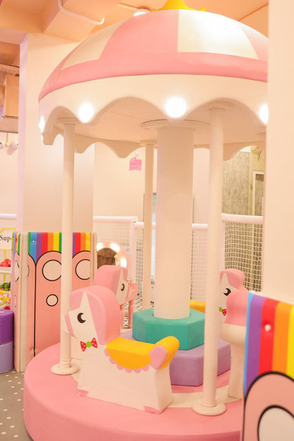 A pink and white carousel with unicorn-shaped seats in a brightly lit play area.