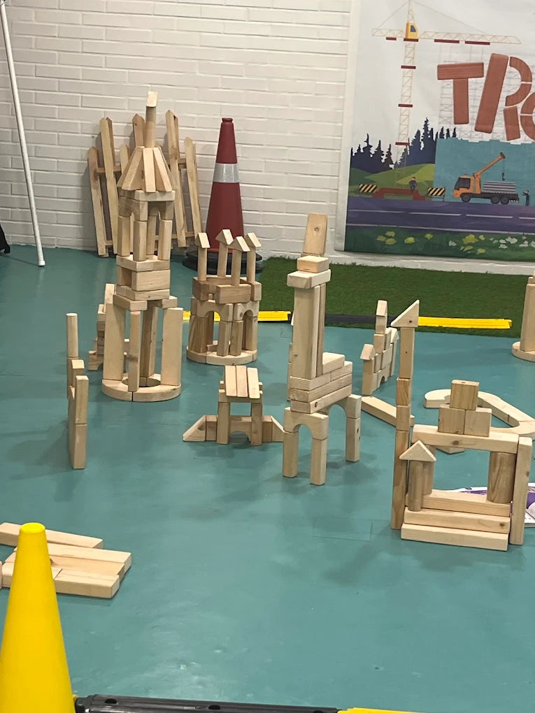 Children's wooden blocks are built into towers and structures on a teal floor, with a construction-themed banner in the background.