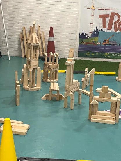 Children's wooden blocks are built into towers and structures on a teal floor, with a construction-themed banner in the background.