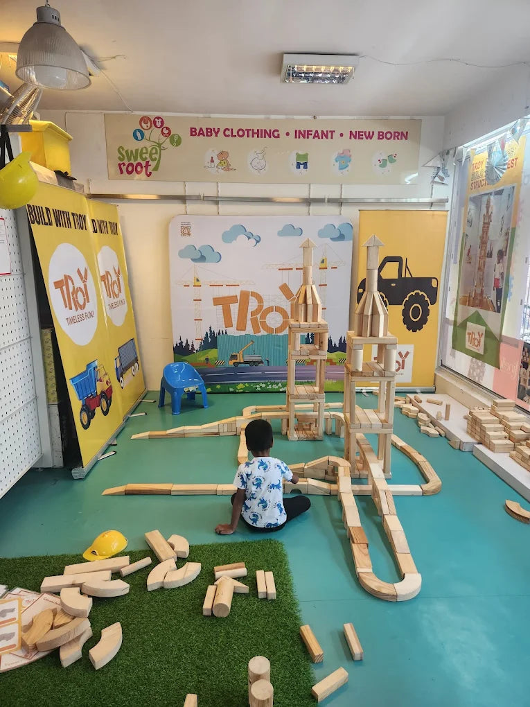 A young child plays with wooden blocks in a room with colorful banners and a construction-themed play area.