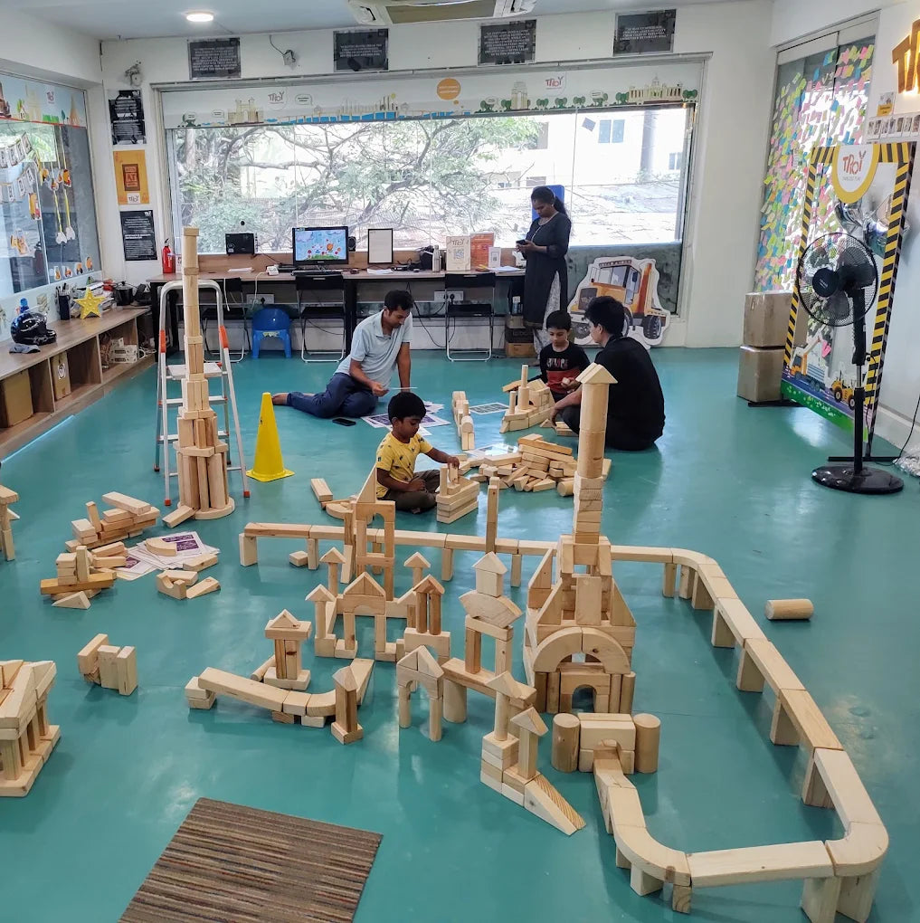 Adults and children play with wooden blocks in a bright, open room.