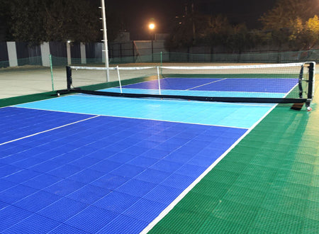 A brightly lit outdoor pickleball court at night with blue and green playing surfaces.