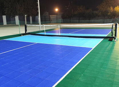 A brightly lit outdoor pickleball court at night with blue and green playing surfaces.