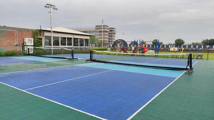 Outdoor pickleball courts with nets, a building, and a playground in the background.