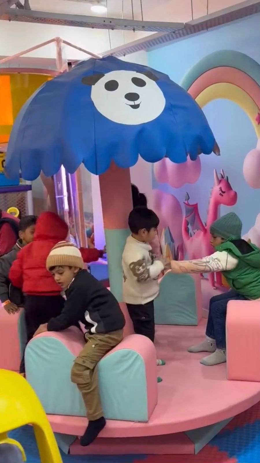Children play in a colorful indoor playground with a panda-themed umbrella and a pink dragon decoration.