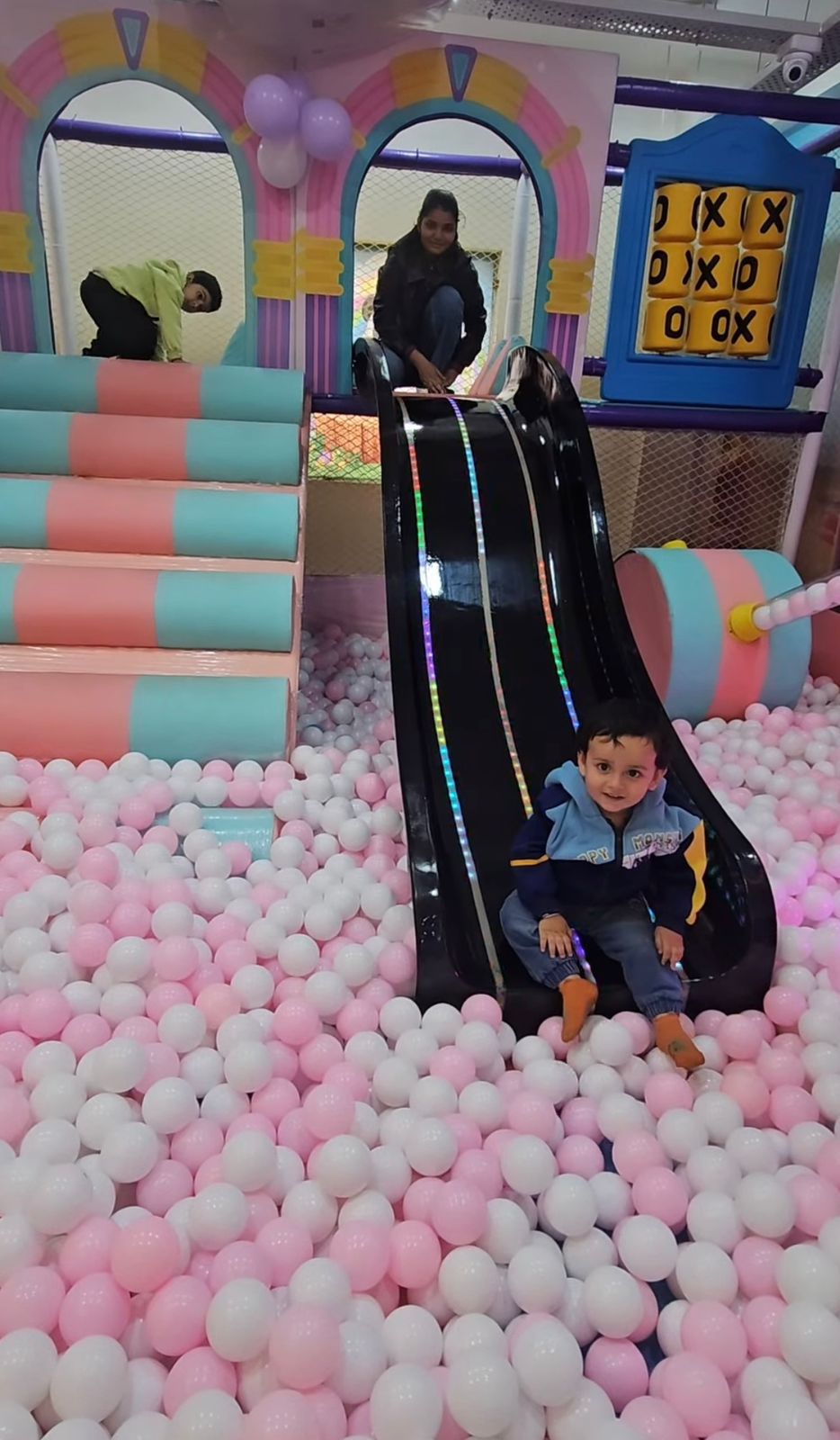 Child sliding down a colorful slide in a play area with pink and white ball pit