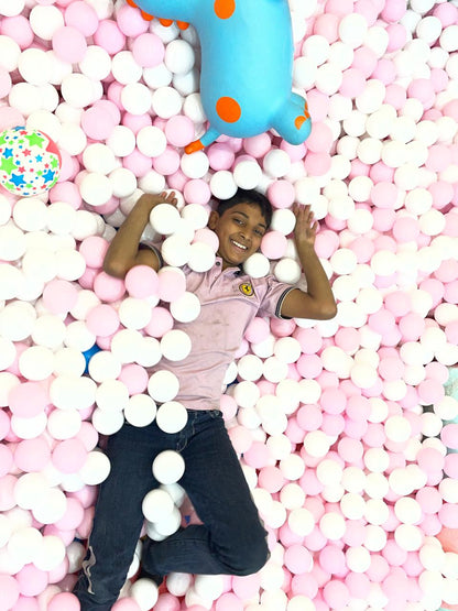 A young boy smiles while lying in a ball pit with pink and white balls.