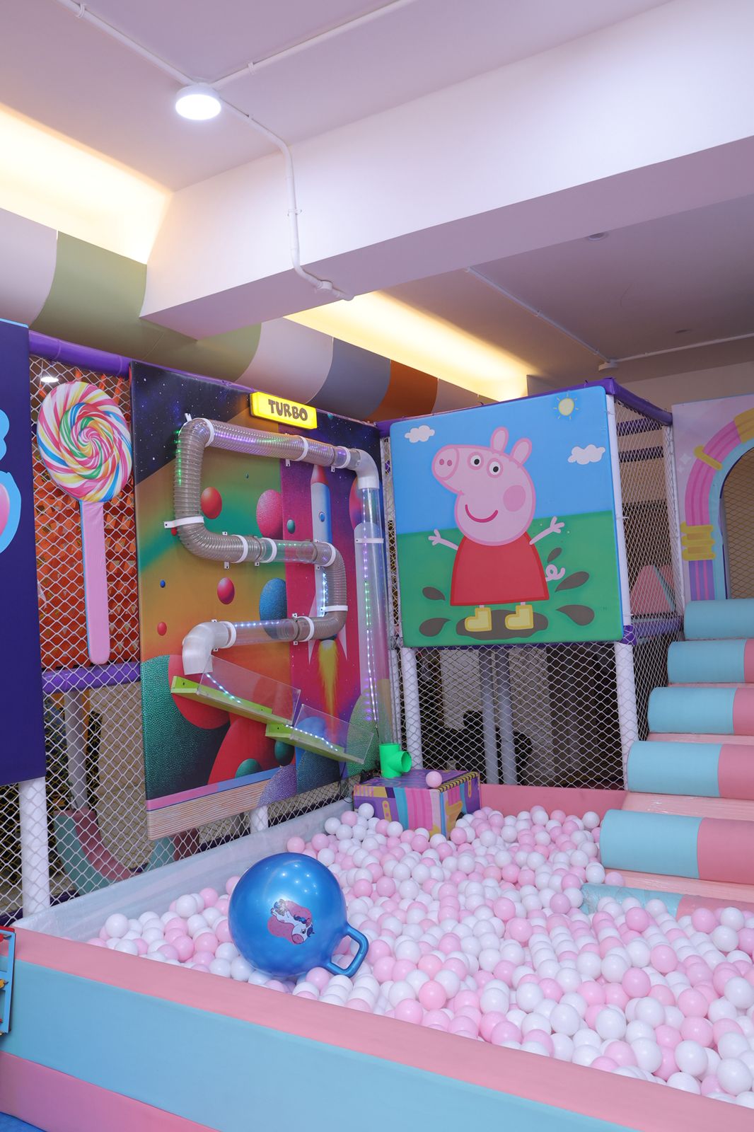 A colorful indoor playground with a ball pit, slides, and Peppa Pig decorations for young children.