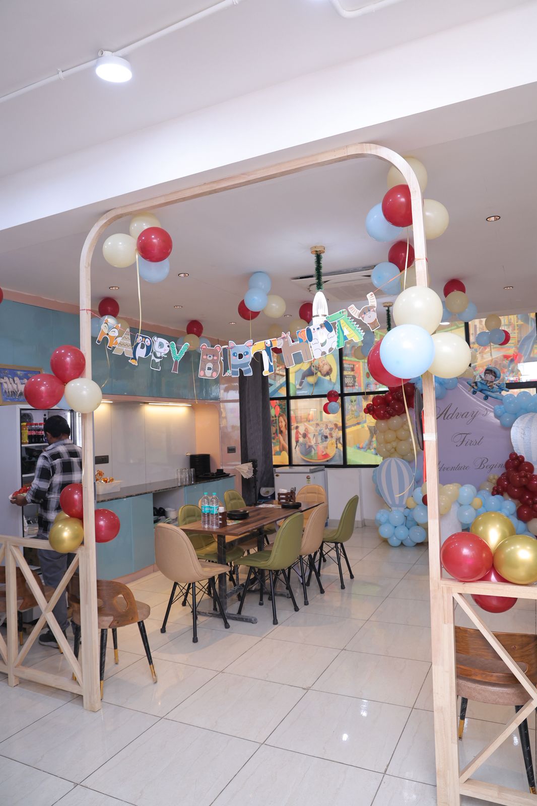 A birthday party setup with balloons and a banner in a restaurant, with a person preparing food.