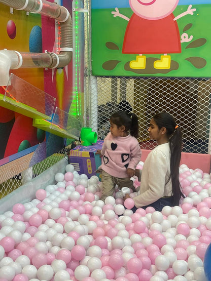 Two young children play in a ball pit with pink and white balls.