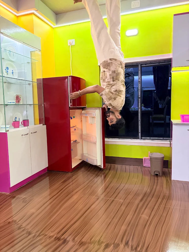 An upside-down young man in a kitchen with bright green walls and a red refrigerator.