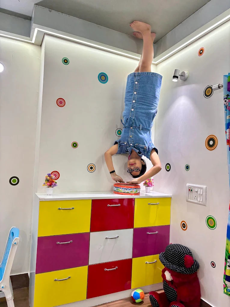 A young girl does a handstand in a room with colorful decorations and furniture.