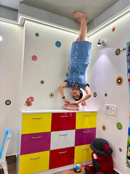 A young girl does a handstand in a room with colorful decorations and furniture.