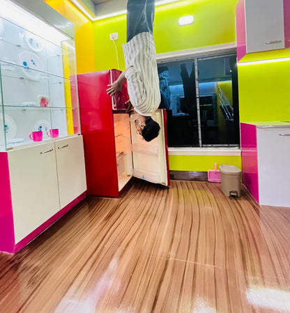 An upside-down person reaches into an open red refrigerator in a brightly colored kitchen.