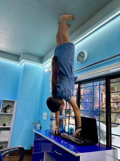 A young person does a handstand on a desk, using a laptop.