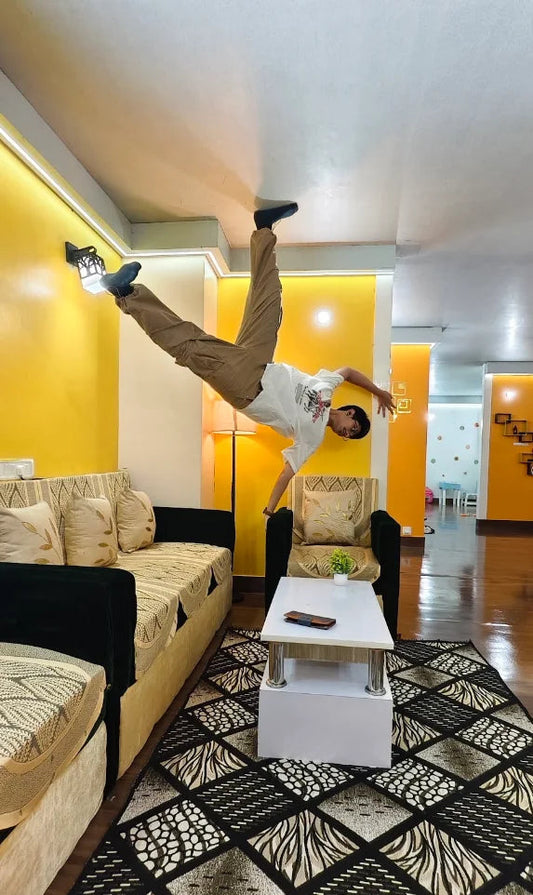 A young person does a handstand on the ceiling in a living room.