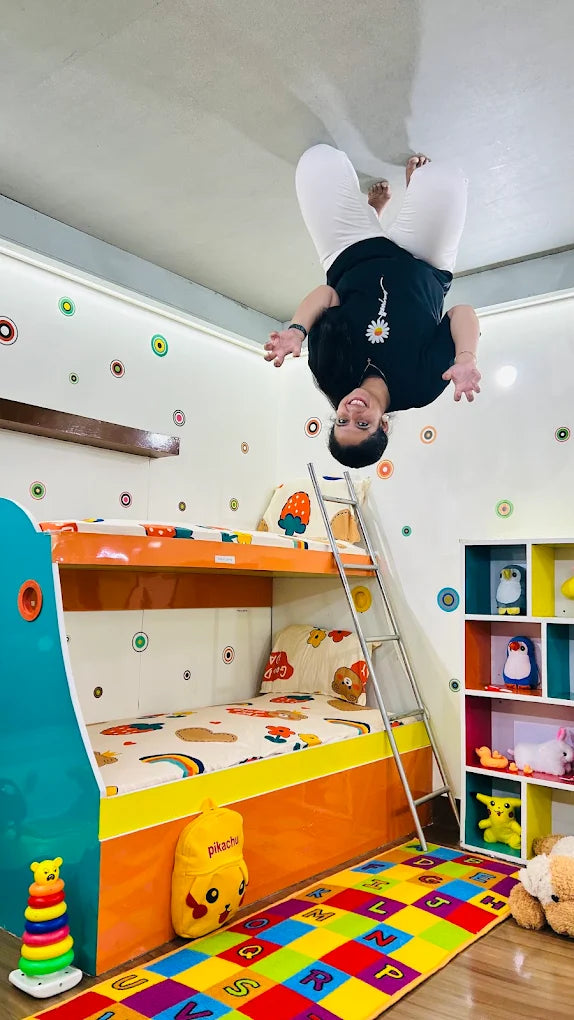 A young person is upside down on the ceiling of a colorful bedroom with bunk beds.