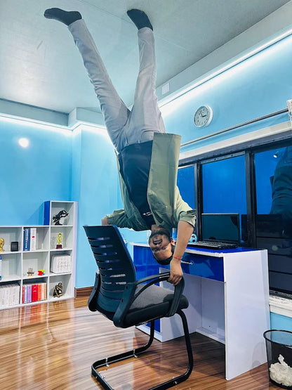 A young man performs a handstand on an office chair, with his feet touching the ceiling.
