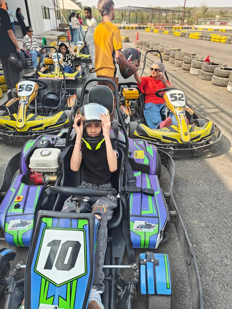 Children and adults in go-karts at a race track, some wearing helmets.