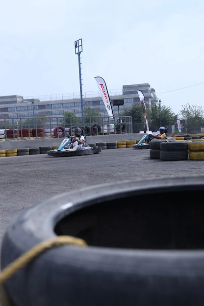 Two children race go-karts on a track with tire barriers and sponsor flags.