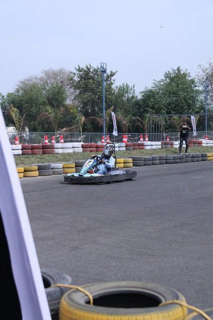 A person in a go-kart races on a track, with a spectator watching in the background.