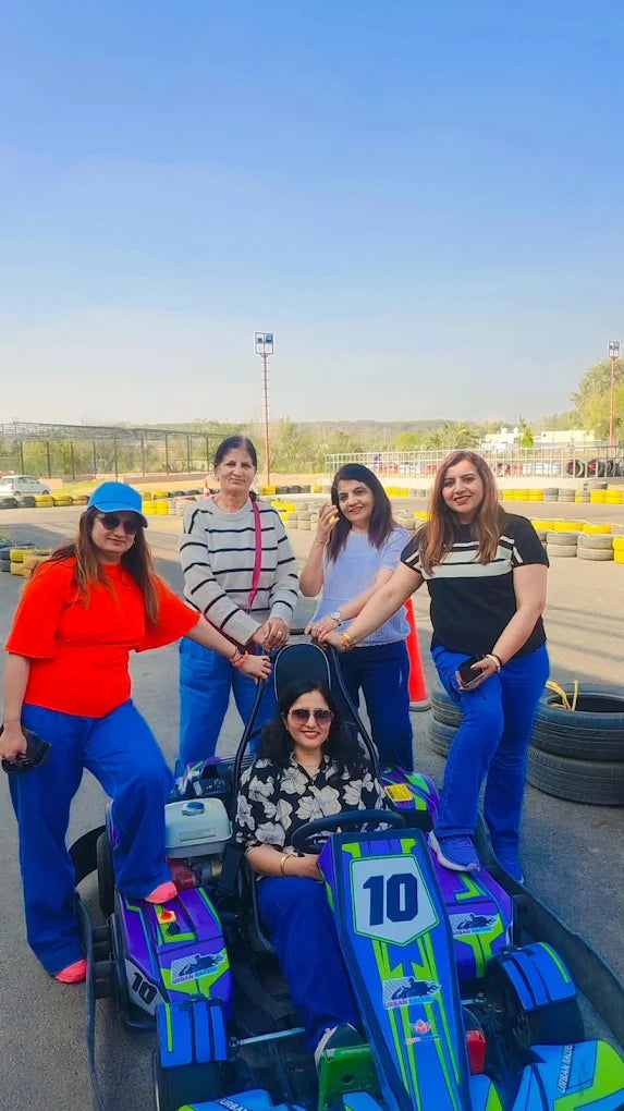 Four women pose with a go-kart at an outdoor track.