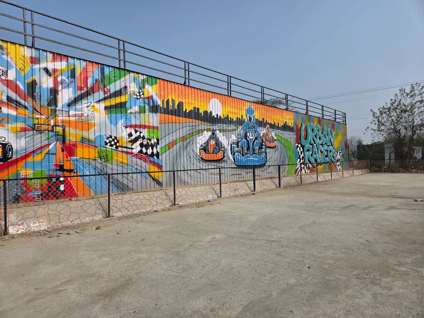 Graffiti art of go-karts racing on a track with a cityscape and sunset.