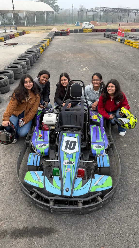 Young women pose with a go-kart on a race track.