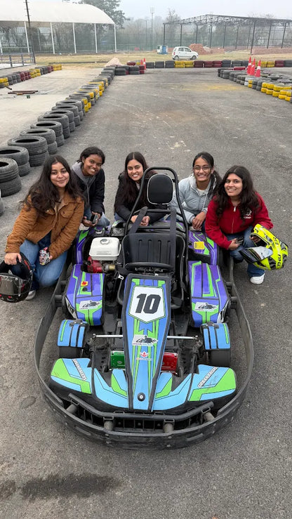 Young women pose with a go-kart on a race track.