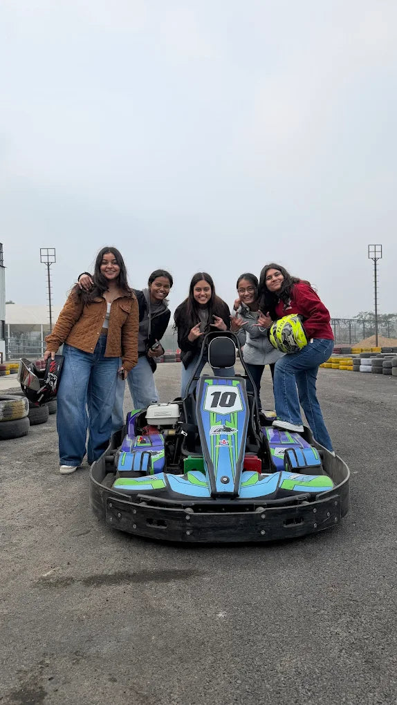 Five young women pose with a go-kart on a track.