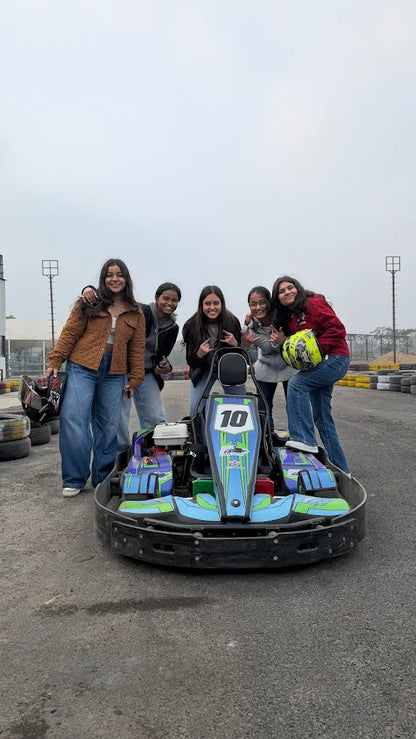 Five young women pose with a go-kart on a track.