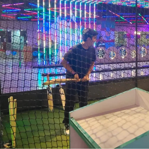 Person playing a batting cage game in an indoor amusement center with colorful lights.
