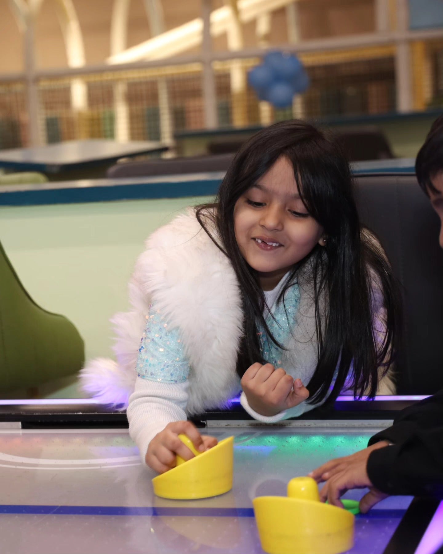 Young girl in a sparkly top and white fur vest playing air hockey at Walk to Wonderland Chhatarpur play area