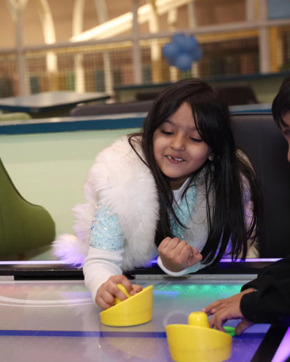 Young girl in a sparkly top and white fur vest playing air hockey at Walk to Wonderland Chhatarpur play area