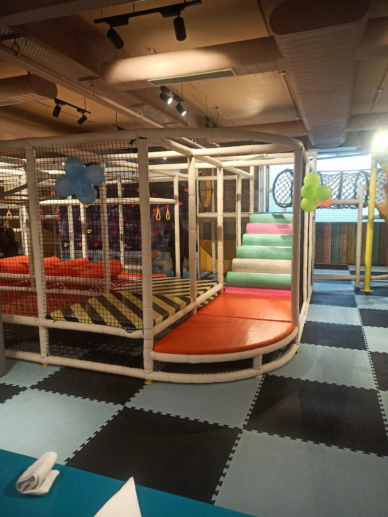 Indoor play structure with soft stairs and climbing net decorated with balloon clusters at Chhatarpur venue