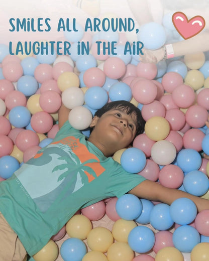 Young boy lying relaxed in a pastel-colored ball pit with a visible wristband at Walk to Wonderland Chhatarpur