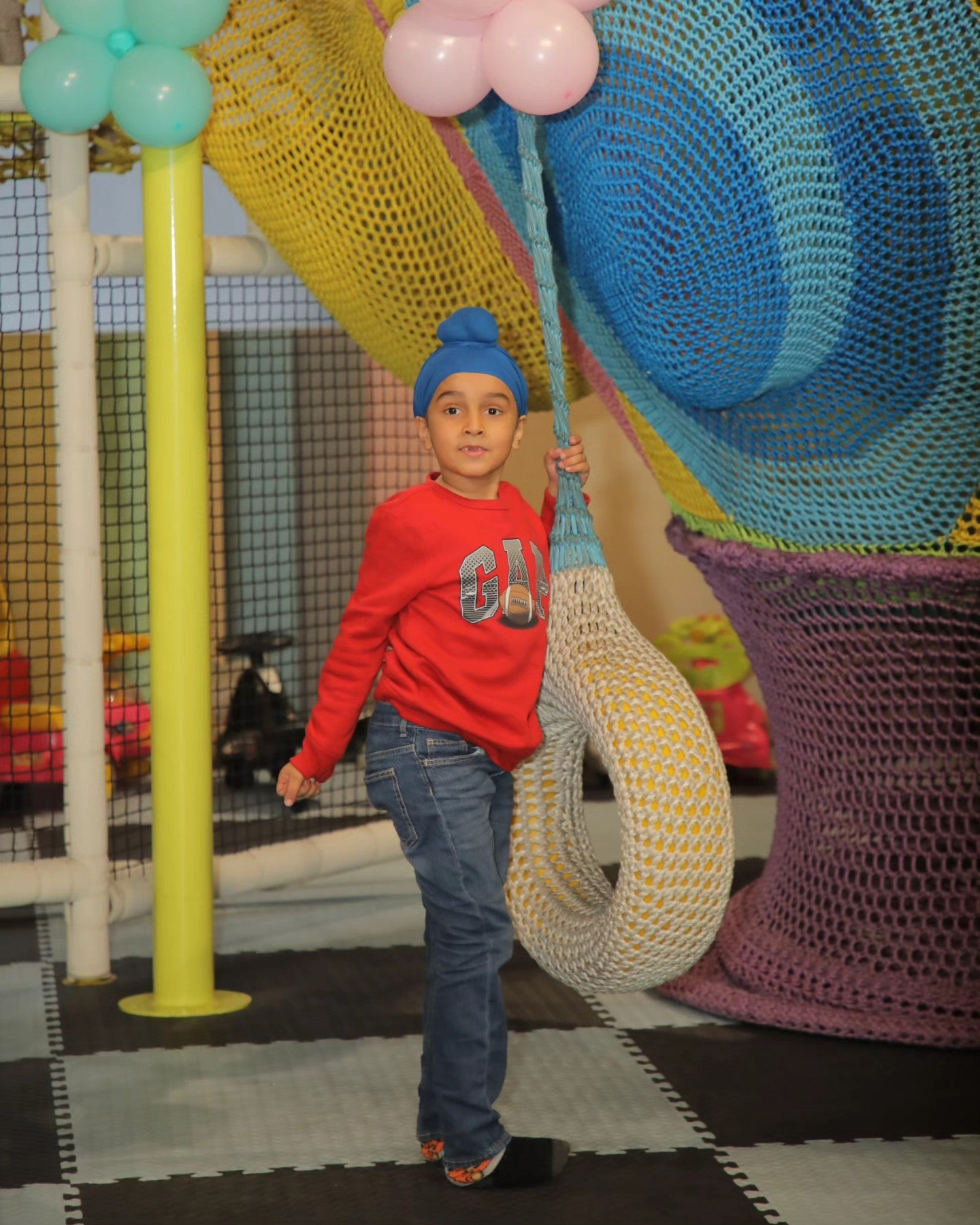 Child in blue turban holding a woven swing in colorful netted play structures at Walk to Wonderland Chhatarpur