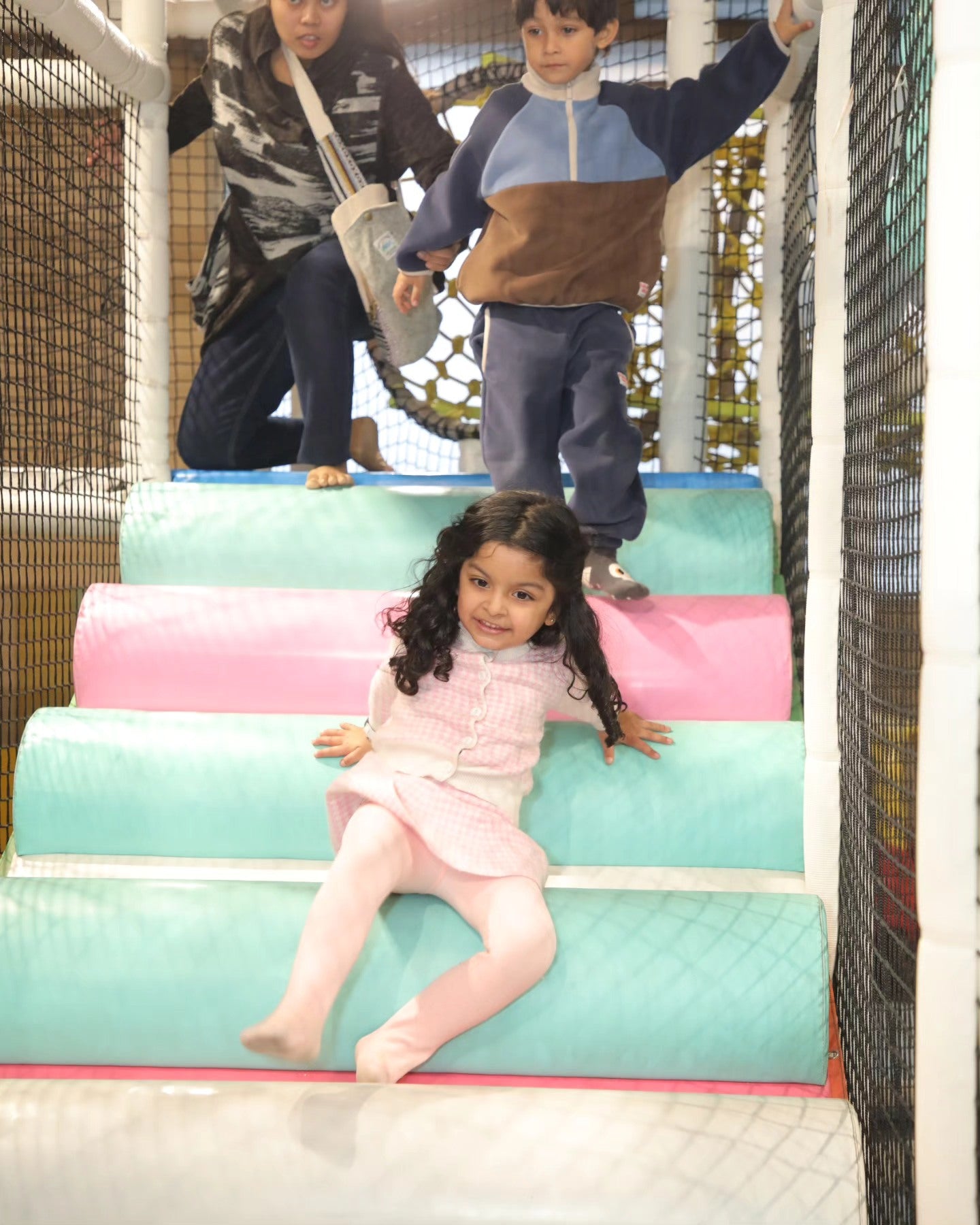 Child sliding down pastel padded steps while another child and adult watch inside Walk to Wonderland Chhatarpur