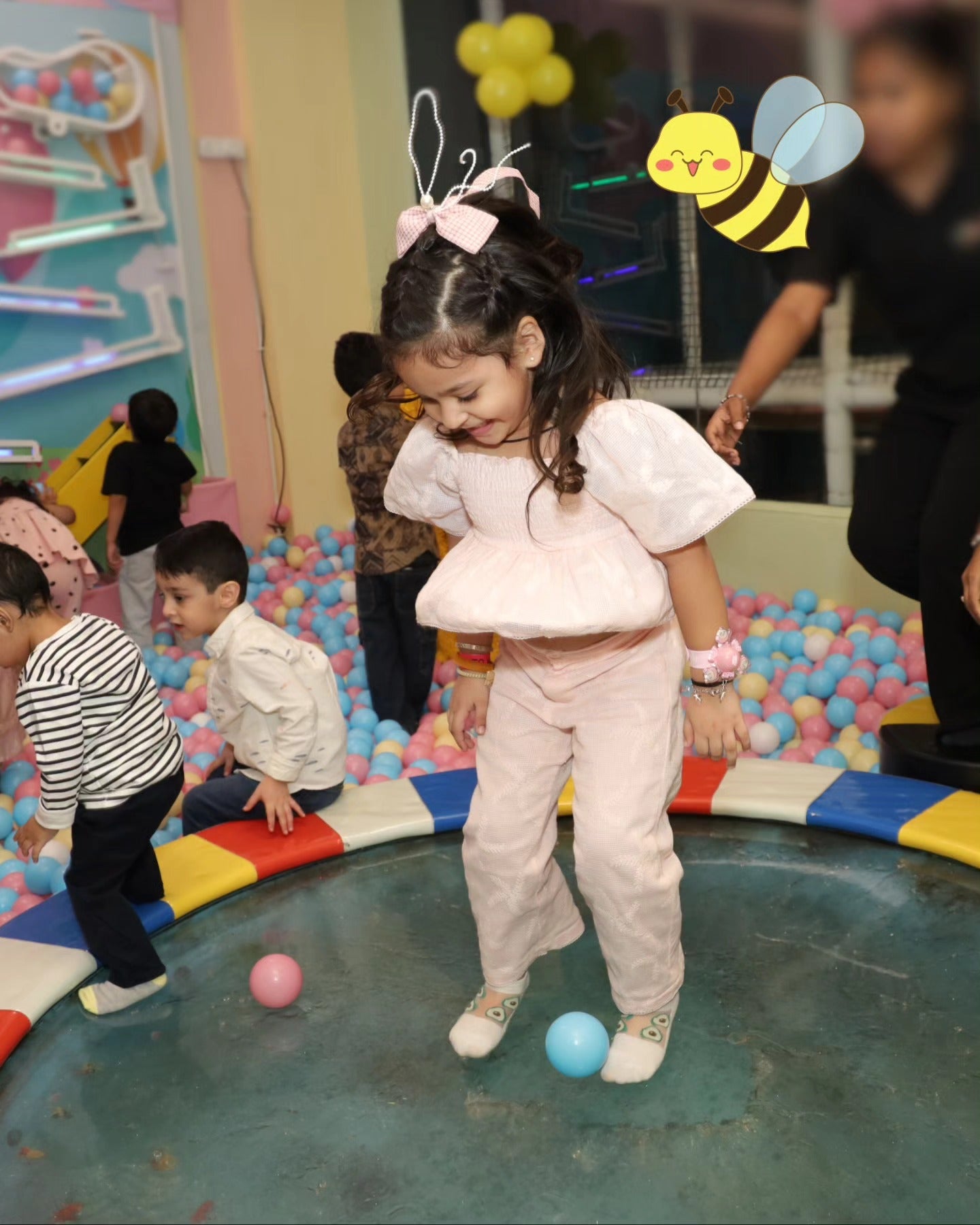Little girl dressed in pink bouncing gently on a colorful trampoline surrounded by pastel ball pit at Chhatarpur play area
