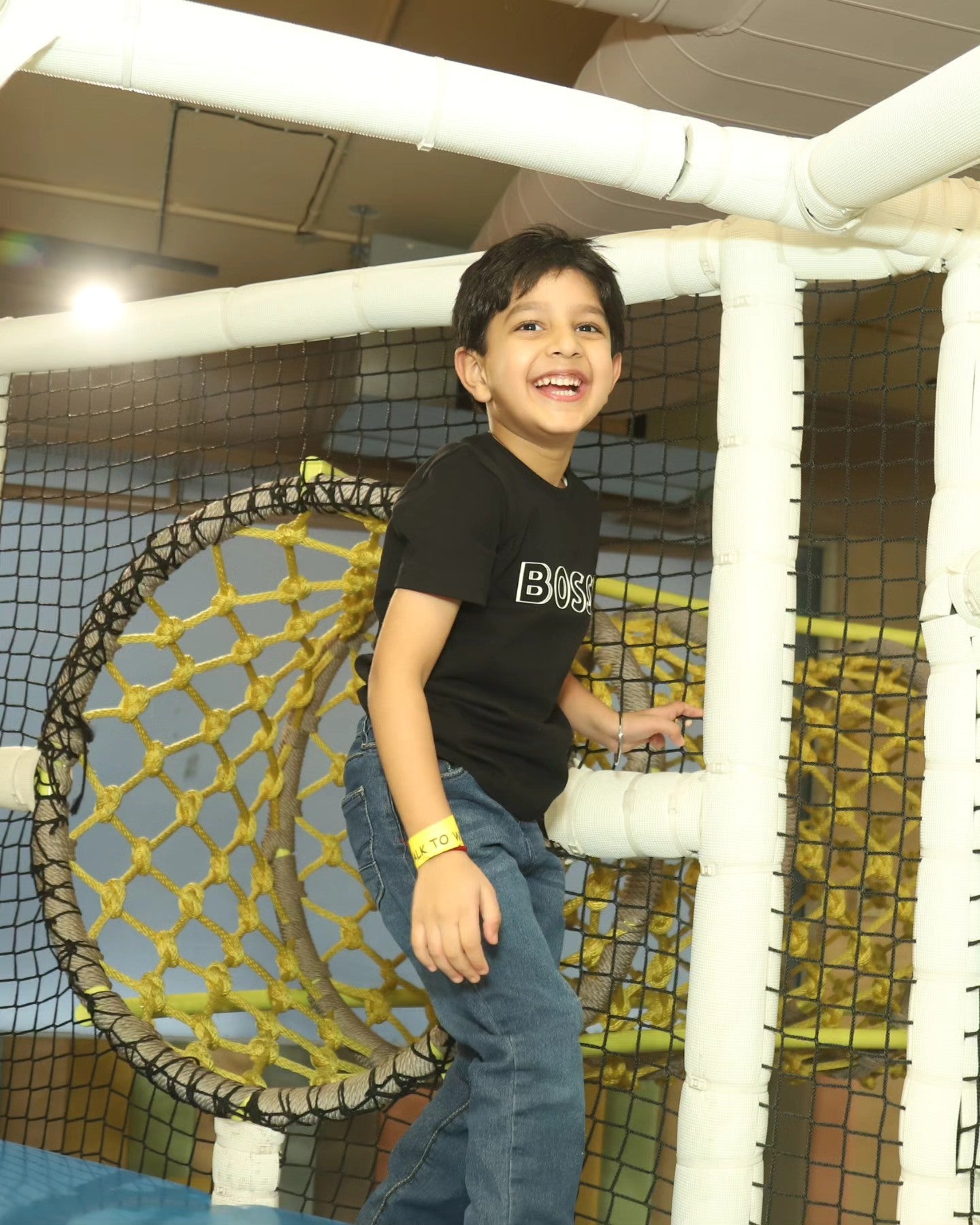 Young boy smiling while climbing a circular rope tunnel in the indoor play area at Chhatarpur New Delhi