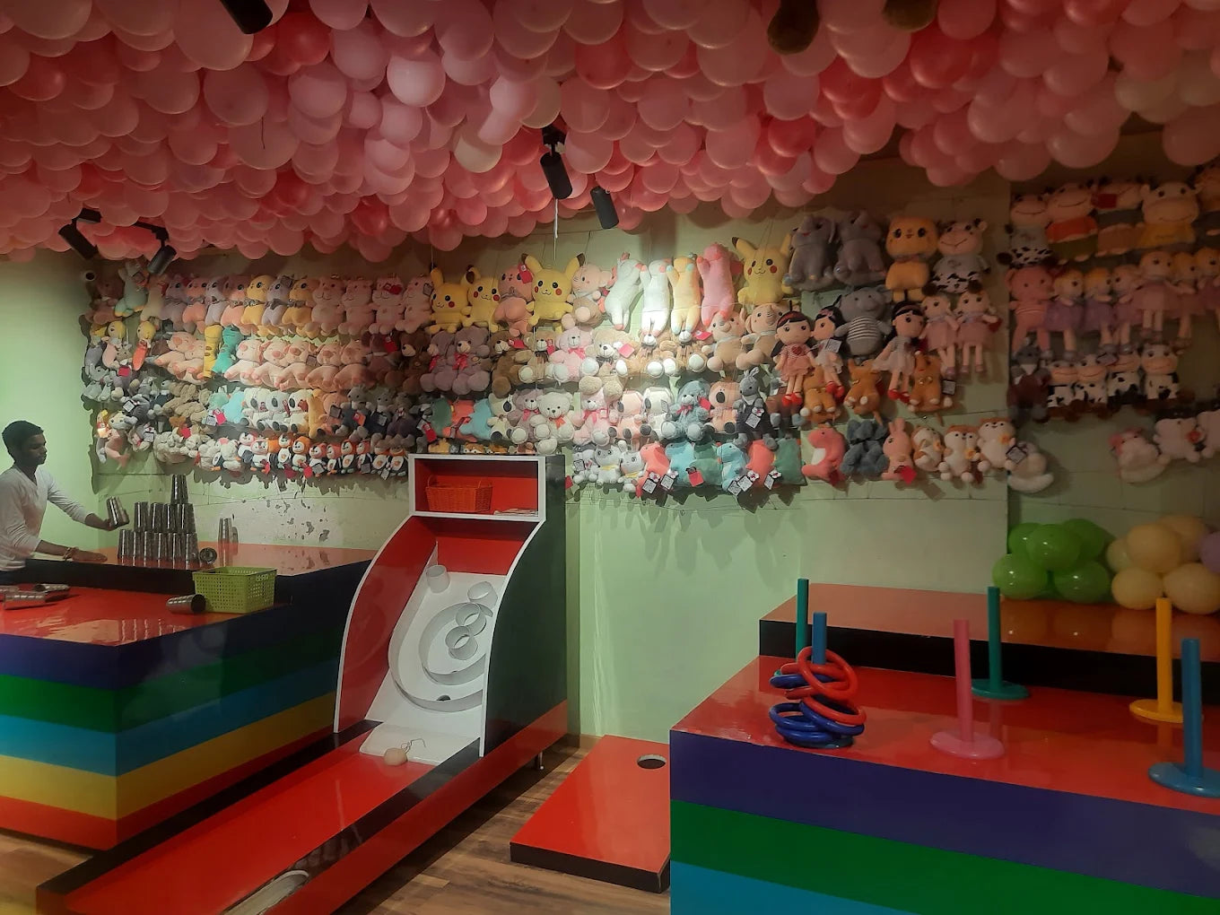 Indoor play area with colorful ring toss game and slide under pink balloon ceiling at Chhatarpur venue