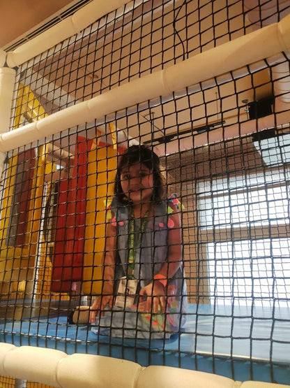 Young child wearing colorful outfit playing behind protective netting inside Walk to Wonderland Chhatarpur play area