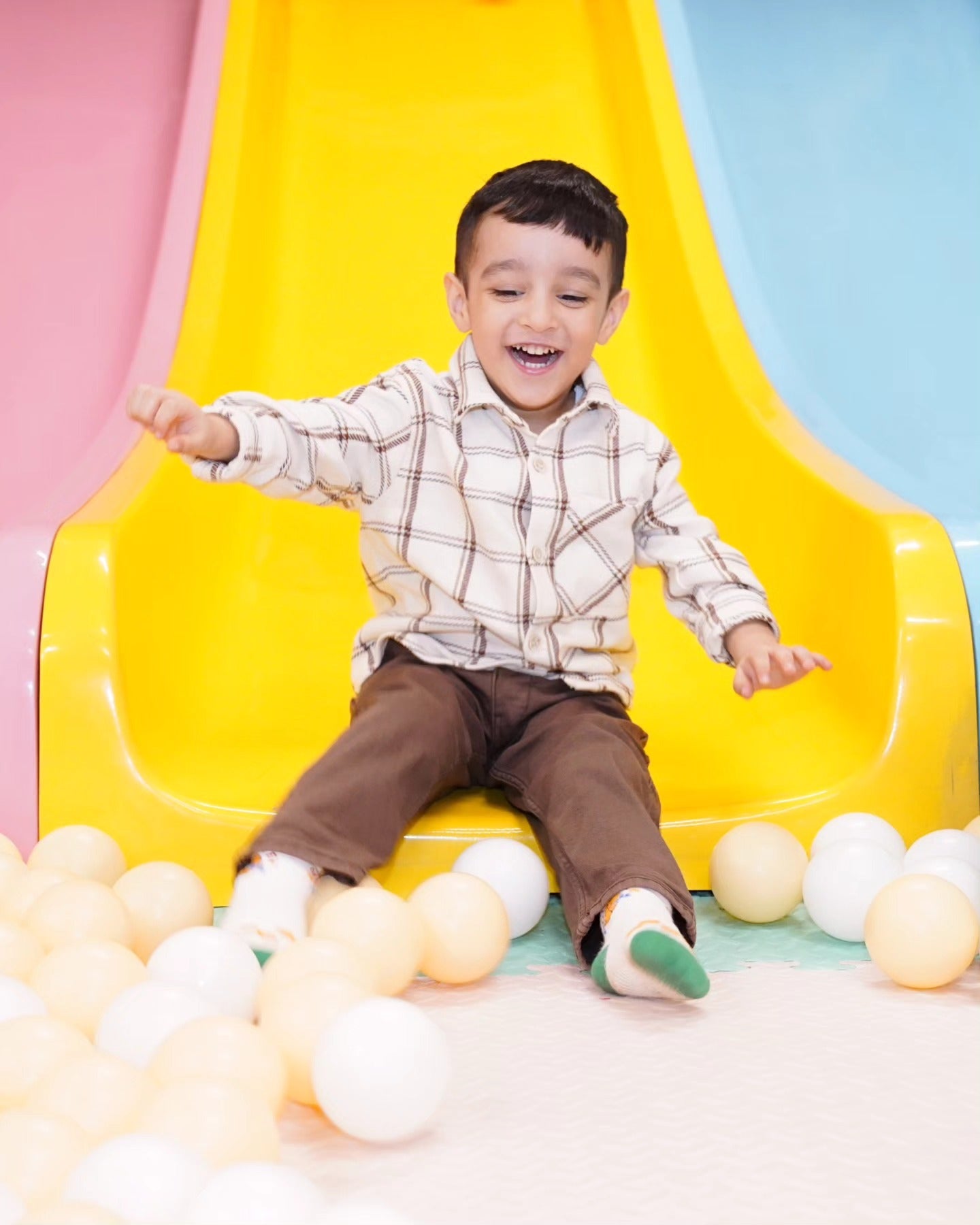 Happy young boy sliding down a bright yellow slide into soft beige and white balls at Walk to Wonderland Chhatarpur