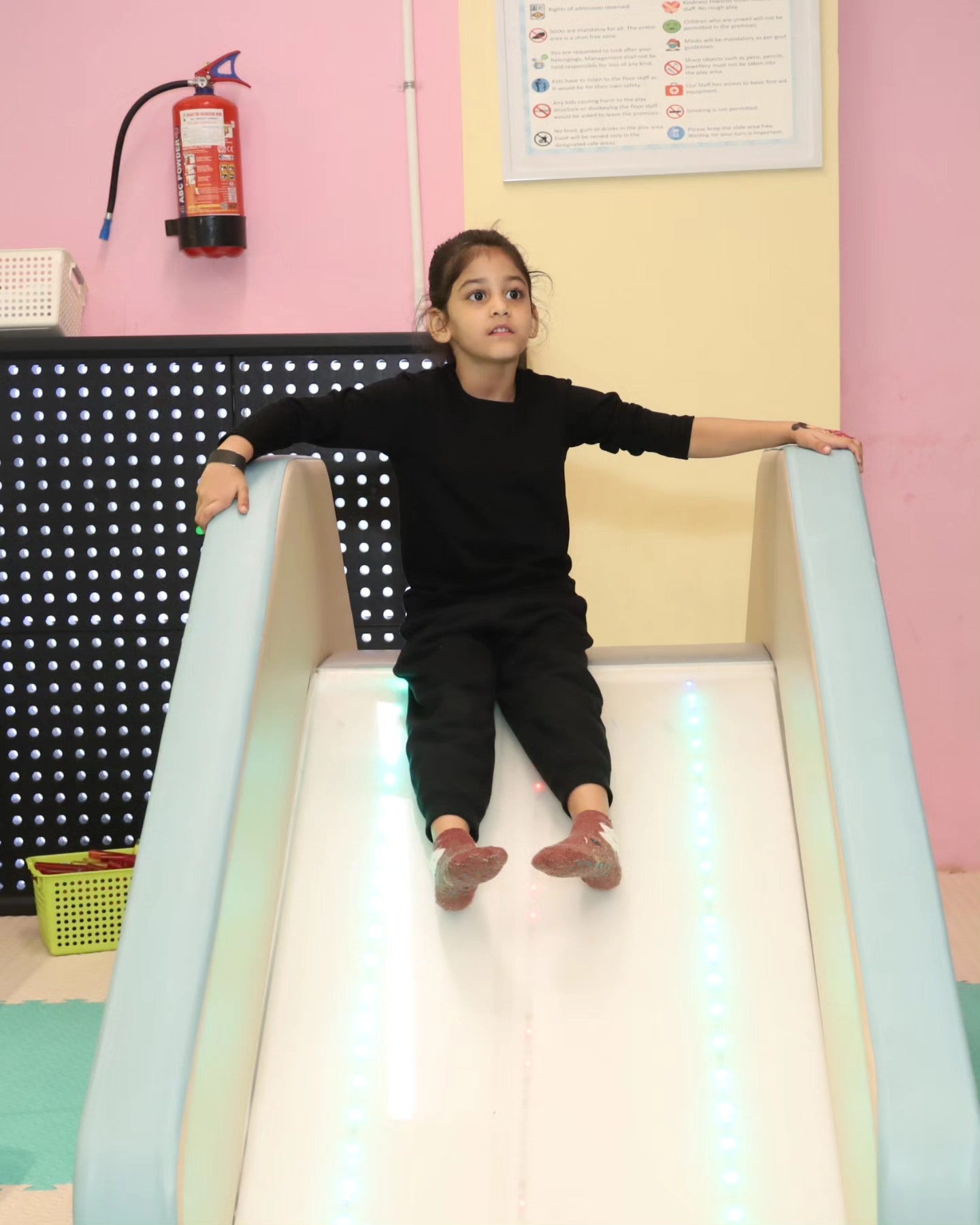 Young child in black outfit sliding down an illuminated white slide inside Walk to Wonderland Chhatarpur play area